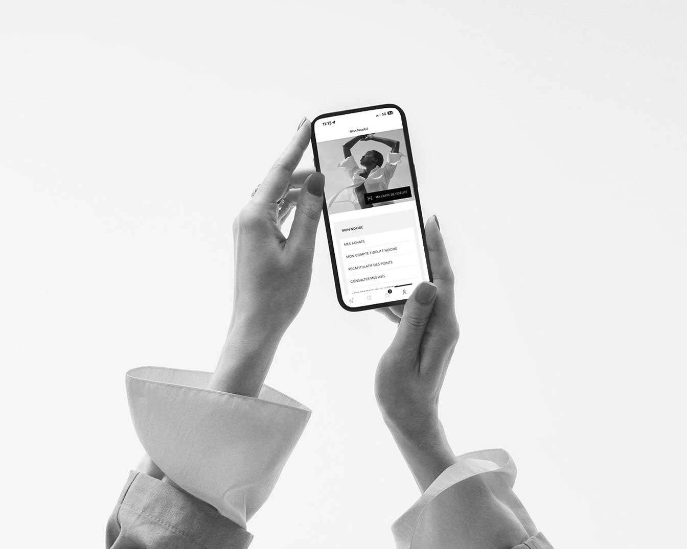 Une femme tient un smartphone affichant l'application Nocibé, avec les options "Mon Nocibé", "Mes achats", "Mon compte fidélité Nocibé", "Récapitulatif des points" et "Consulter mes avis" visibles.