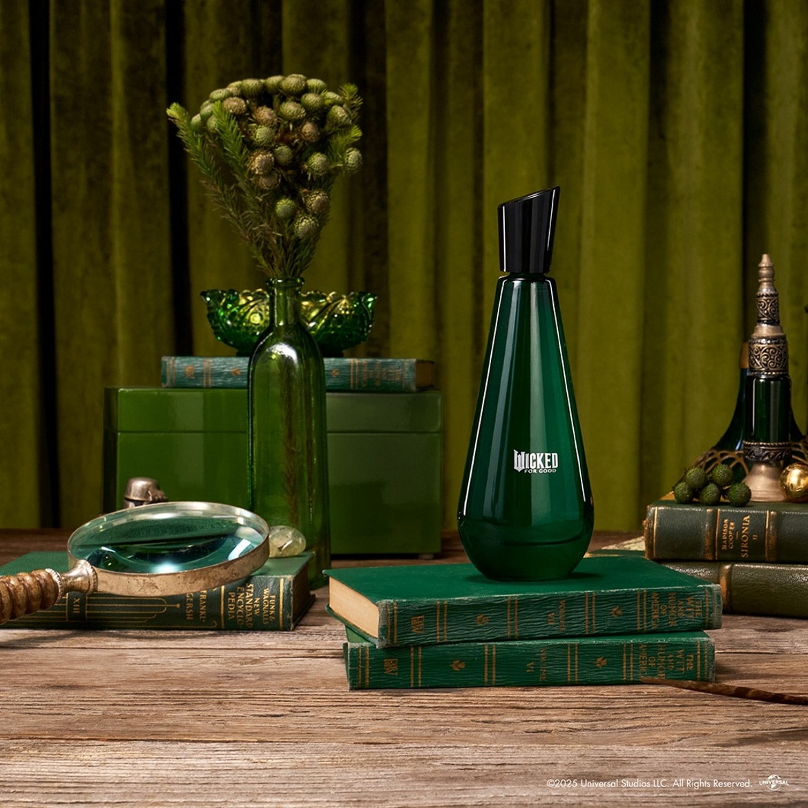 Discover Wicked For Good, a fragrance presented in an elegant green bottle with black accents, displayed among vintage books and decorative green glass.