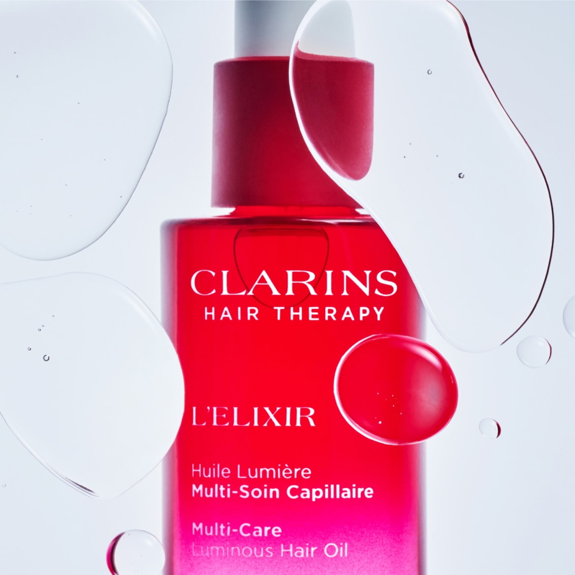 Découvrez l'Huile Lumière Multi-Soin Capillaire L'ELIXIR de Clarins Hair Therapy, un flacon rouge vif avec des gouttes d'huile claires en suspension, pour des cheveux éclatants de santé.