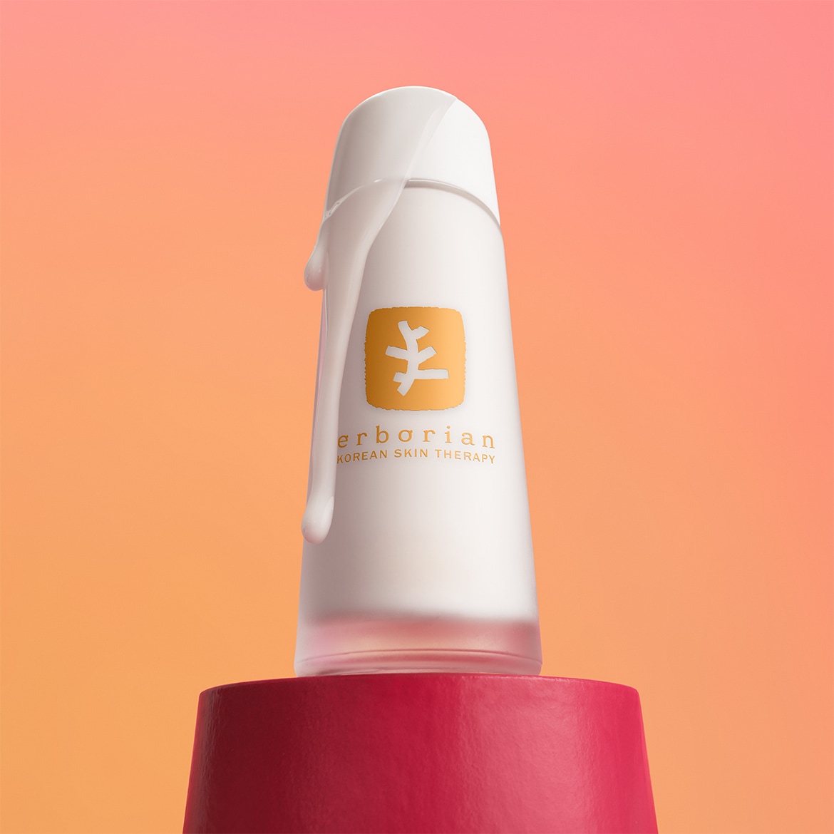 Le flacon blanc givré d'Erborian Korean Skin Therapy, orné d'un logo doré, est mis en valeur sur un socle rouge, avec une texture crémeuse qui coule sur le côté, évoquant la richesse du produit.