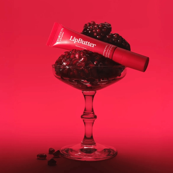 Découvrez le LipButter de KylieSkin, un baume à lèvres rouge présenté dans un verre rempli de graines de grenade, pour une hydratation et une protection optimales.