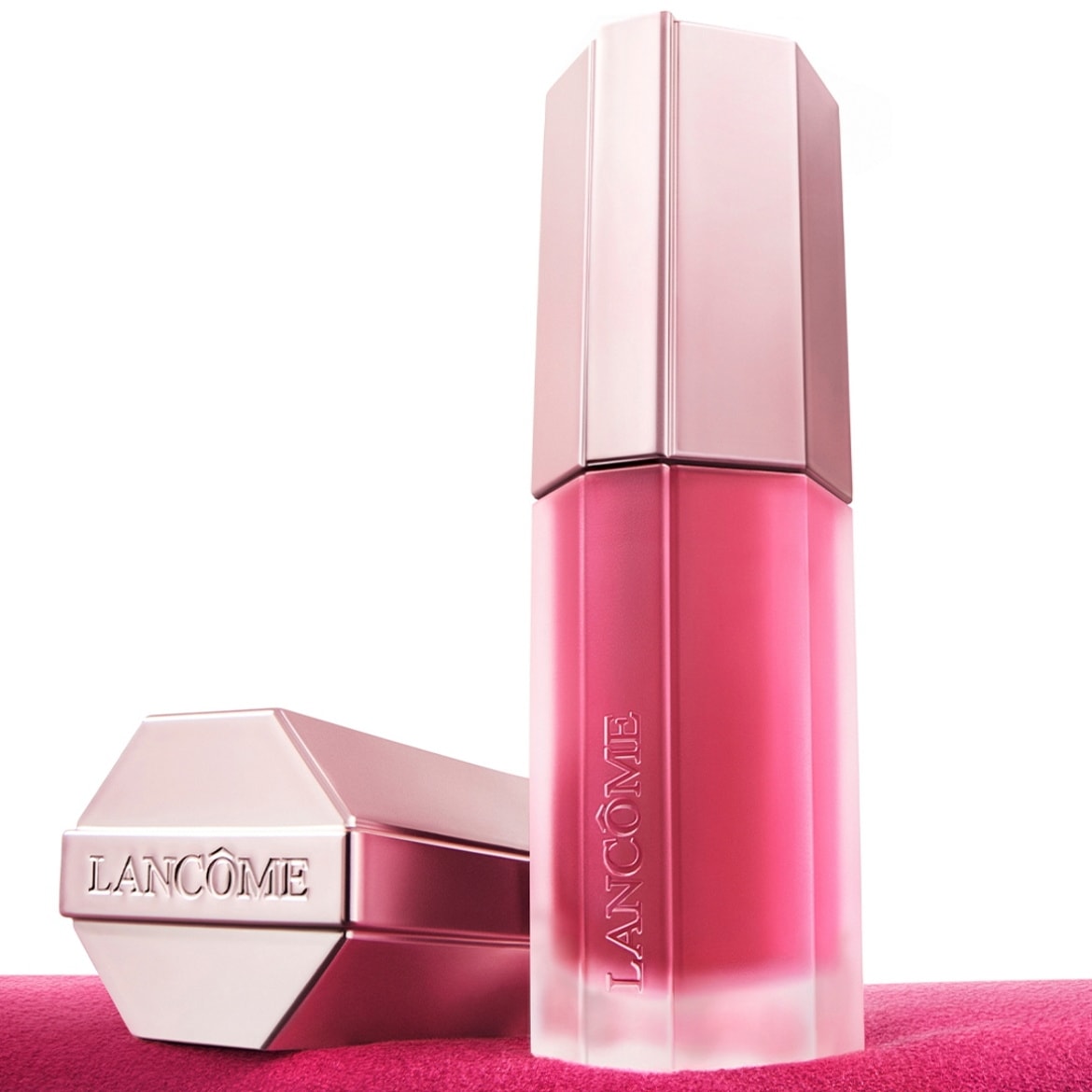 Le brillant à lèvres Lancôme L'Absolu Lacquer en teinte rose vif est présenté avec son capuchon hexagonal assorti, posé sur un tissu rose.