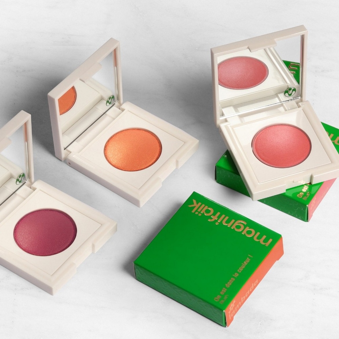 Découvrez les blushs Magnifaïk dans des teintes vibrantes comme le rose, l'orange et le framboise, présentés dans des boîtiers élégants avec miroir intégré et emballages verts.