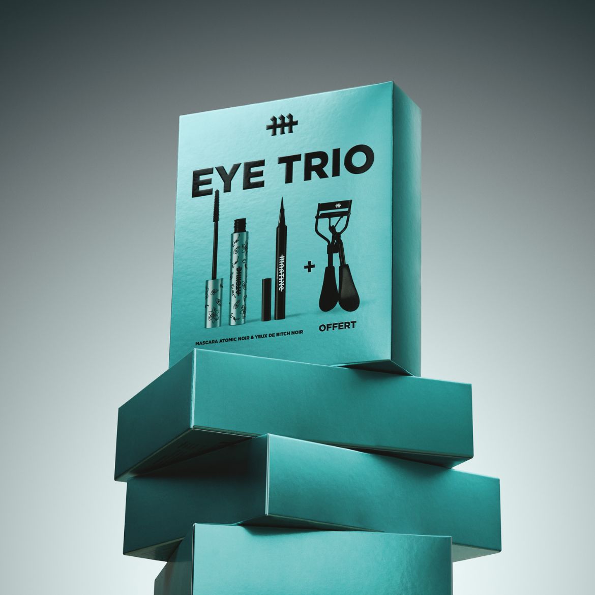 Découvrez l'ensemble Eye Trio dans un emballage bleu turquoise, comprenant un mascara Atomic Noir, un eye-liner et un recourbe-cils, le tout présenté sur une pile de boîtes.