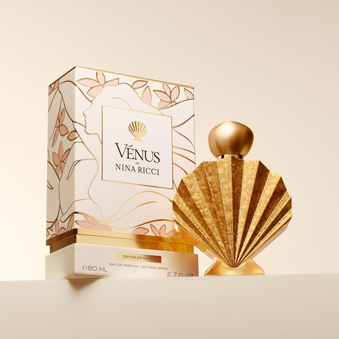 Découvrez Vénus de Nina Ricci Édition Or Nacrée, une eau de parfum en vaporisateur naturel de 80 ml, présentée dans un flacon doré en forme de coquillage et un emballage orné de motifs floraux.
