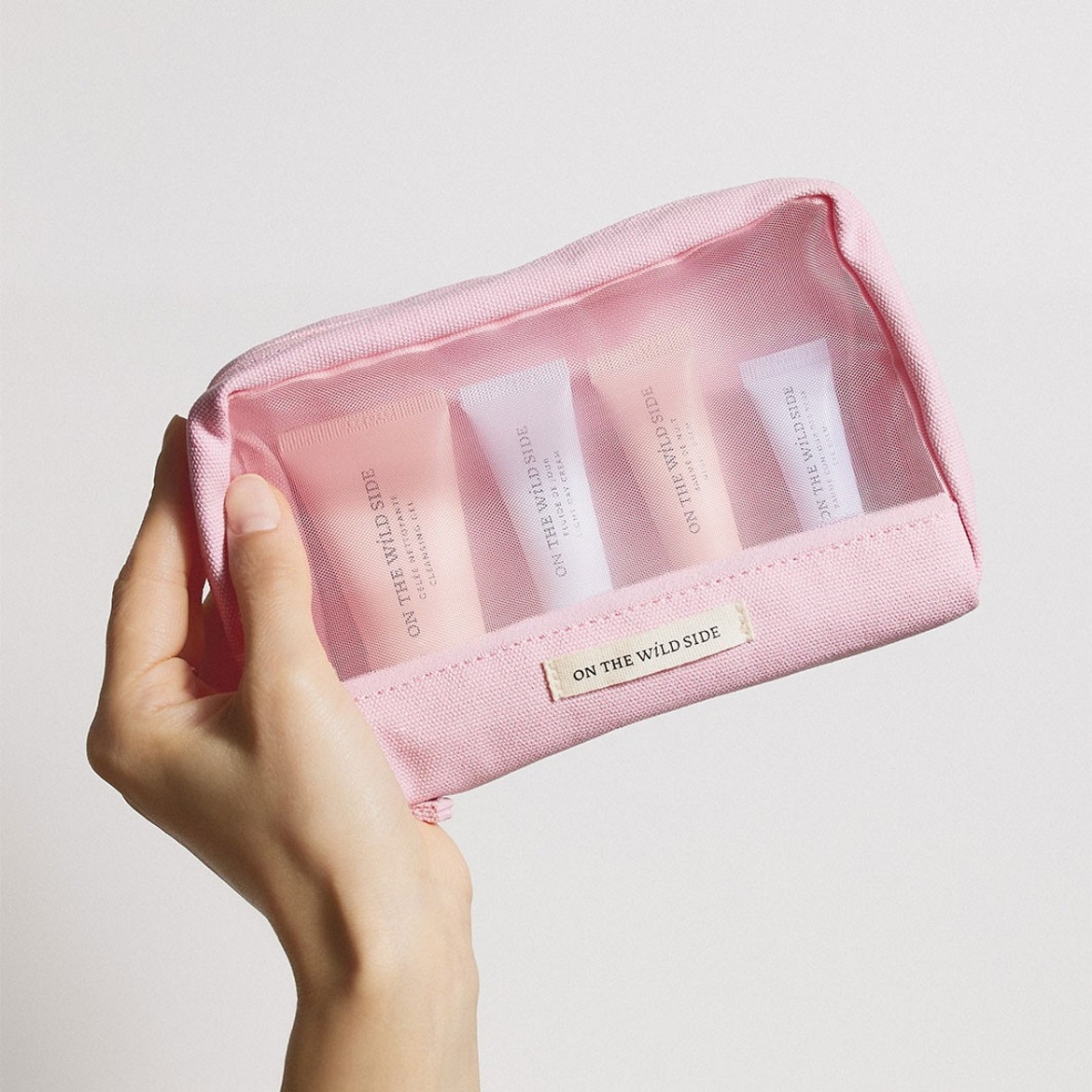 Voici une trousse de toilette rose transparente "ON THE WILD SIDE" contenant une gelée nettoyante, un fluide de jour et une mauve de nuit, parfaits pour vos essentiels de voyage.