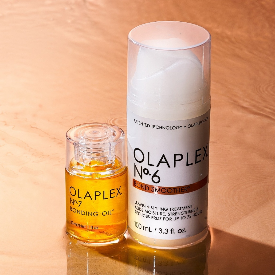 L'image présente deux produits Olaplex : l'huile de liaison n°7, un flacon transparent de 30 ml avec un liquide doré, et le Bond Smoother n°6, un flacon blanc de 100 ml avec une pompe, tous deux posés sur une surface cuivrée.
