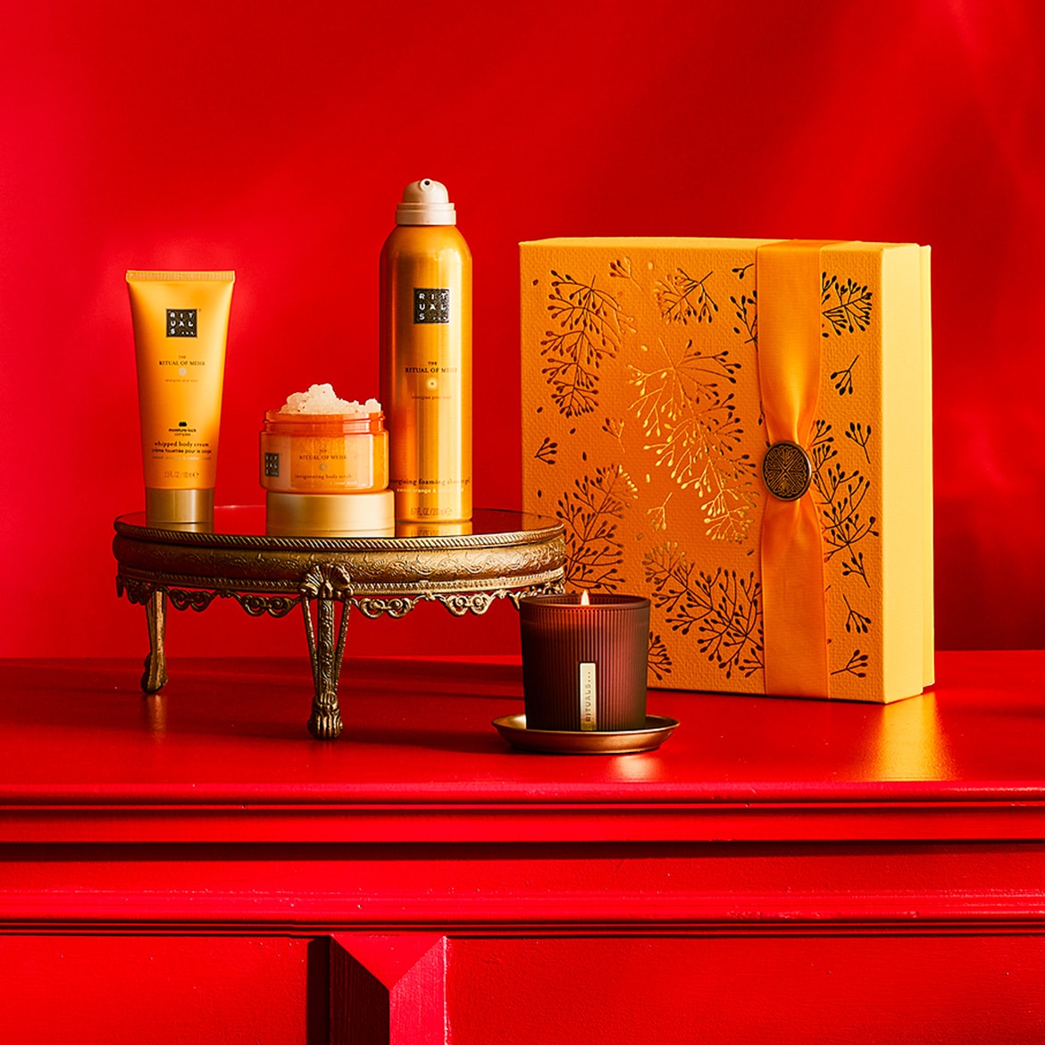 Un ensemble de produits de soins corporels Rituals of Mehr, comprenant une crème fouettée, un gommage corporel et une mousse de douche, est présenté sur un plateau doré.