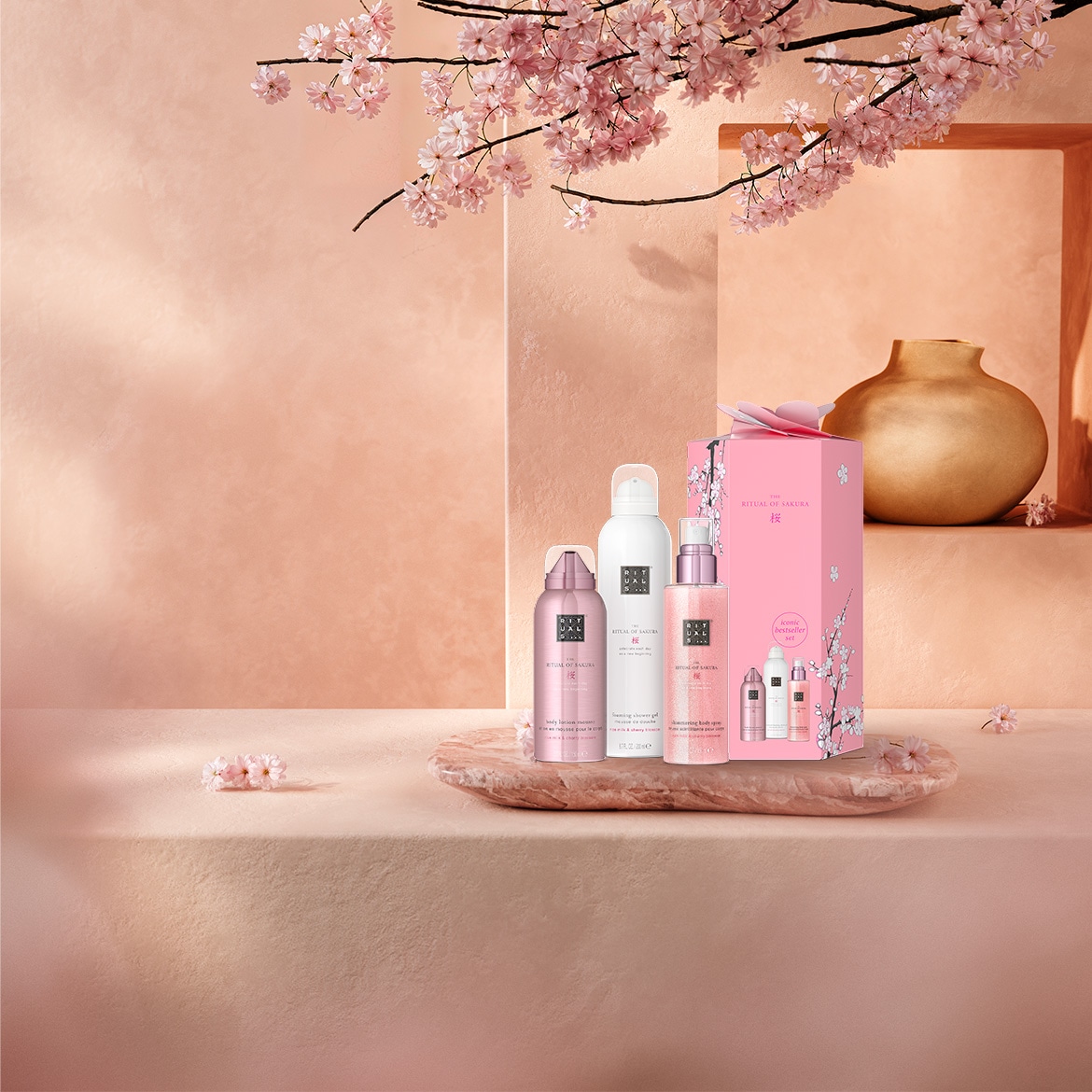 Découvrez le coffret cadeau Ritual of Sakura, comprenant une mousse de douche, un gommage corporel, une crème pour le corps et un parfum d'intérieur, le tout dans un emballage rose orné de fleurs de cerisier.
