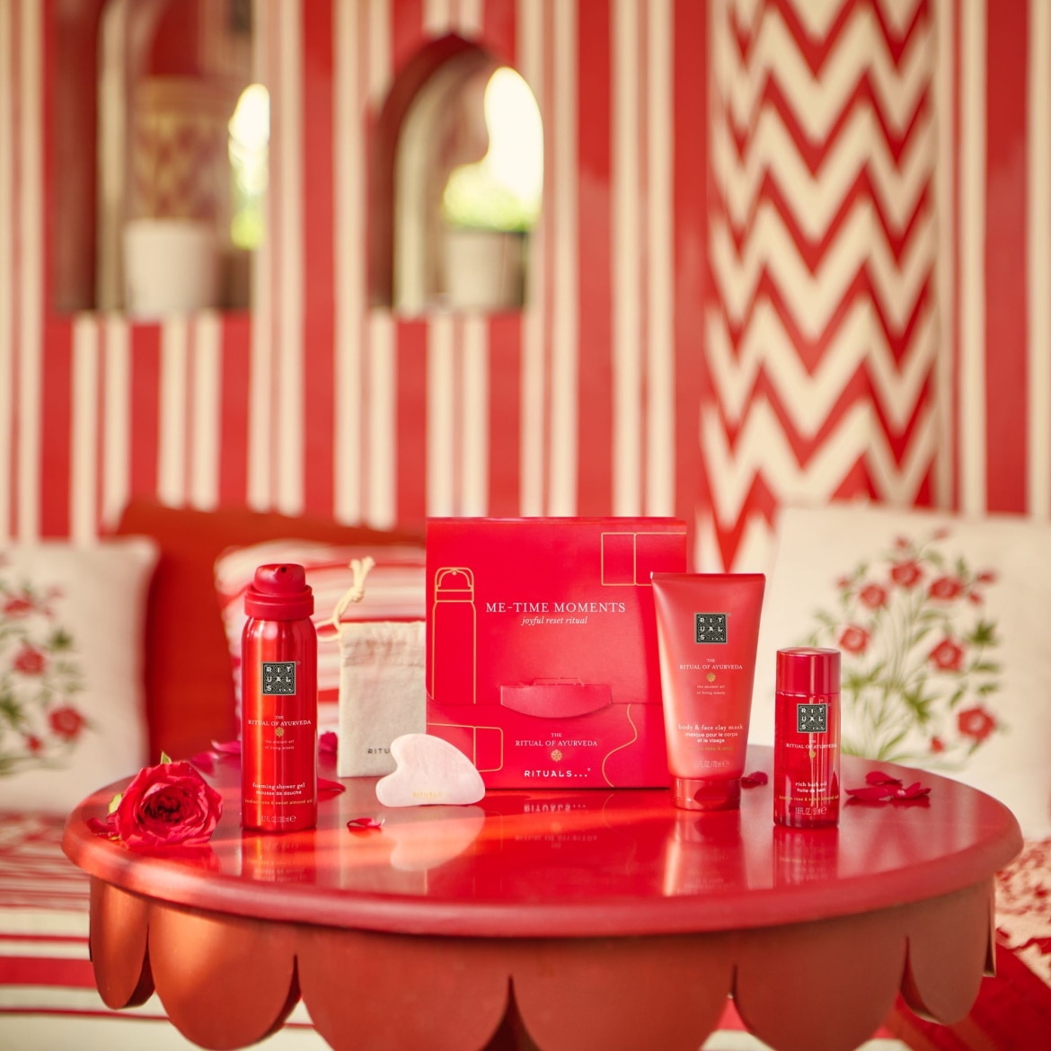Découvrez le coffret rouge « ME-TIME MOMENTS joyful reset ritual » de Rituals, comprenant un gel douche moussant, un masque à l'argile pour le corps et le visage, et une huile riche pour le corps, présentés sur une table rouge.