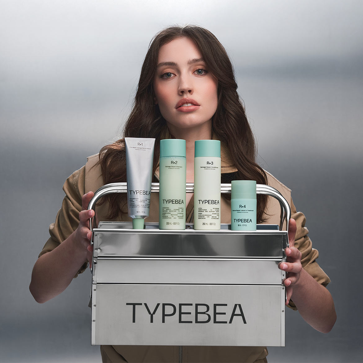 Une femme tient un chariot métallique contenant les produits capillaires TYPEBEA : un masque, un shampooing, un revitalisant et un traitement sans rinçage.