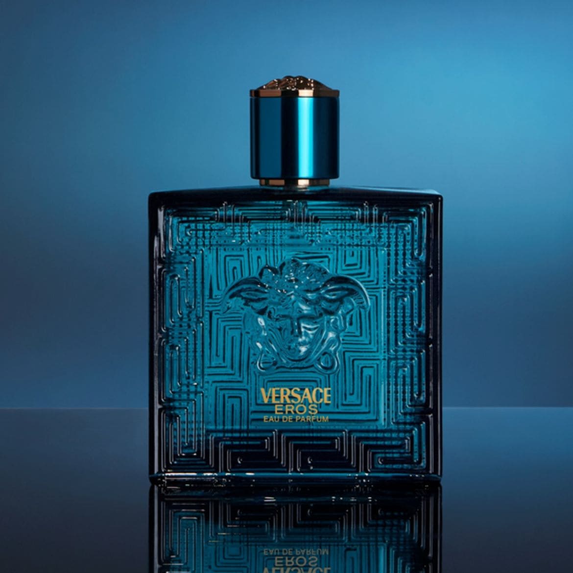 Le parfum Versace Eros Eau de Parfum est présenté dans un flacon rectangulaire en verre bleu sarcelle avec un motif grec en relief et un médaillon de Méduse doré au centre, surmonté d'un bouchon bleu sarcelle et or.