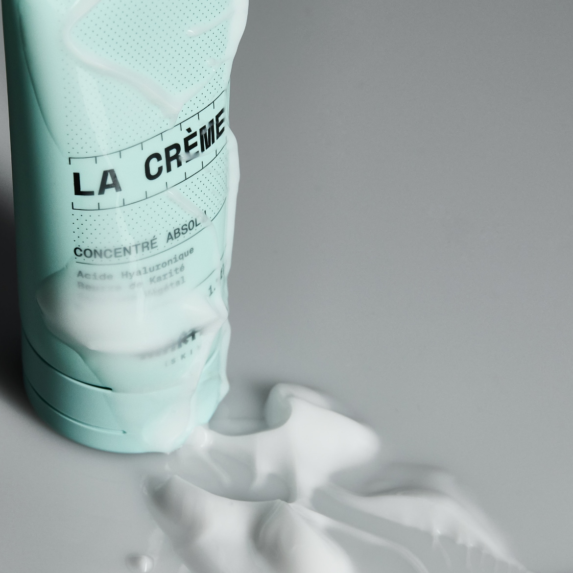 Voici un tube bleu clair de La Crème Concentré Absol, avec une texture crémeuse blanche qui s'étale, promettant une hydratation intense grâce à l'acide hyaluronique et au karité.