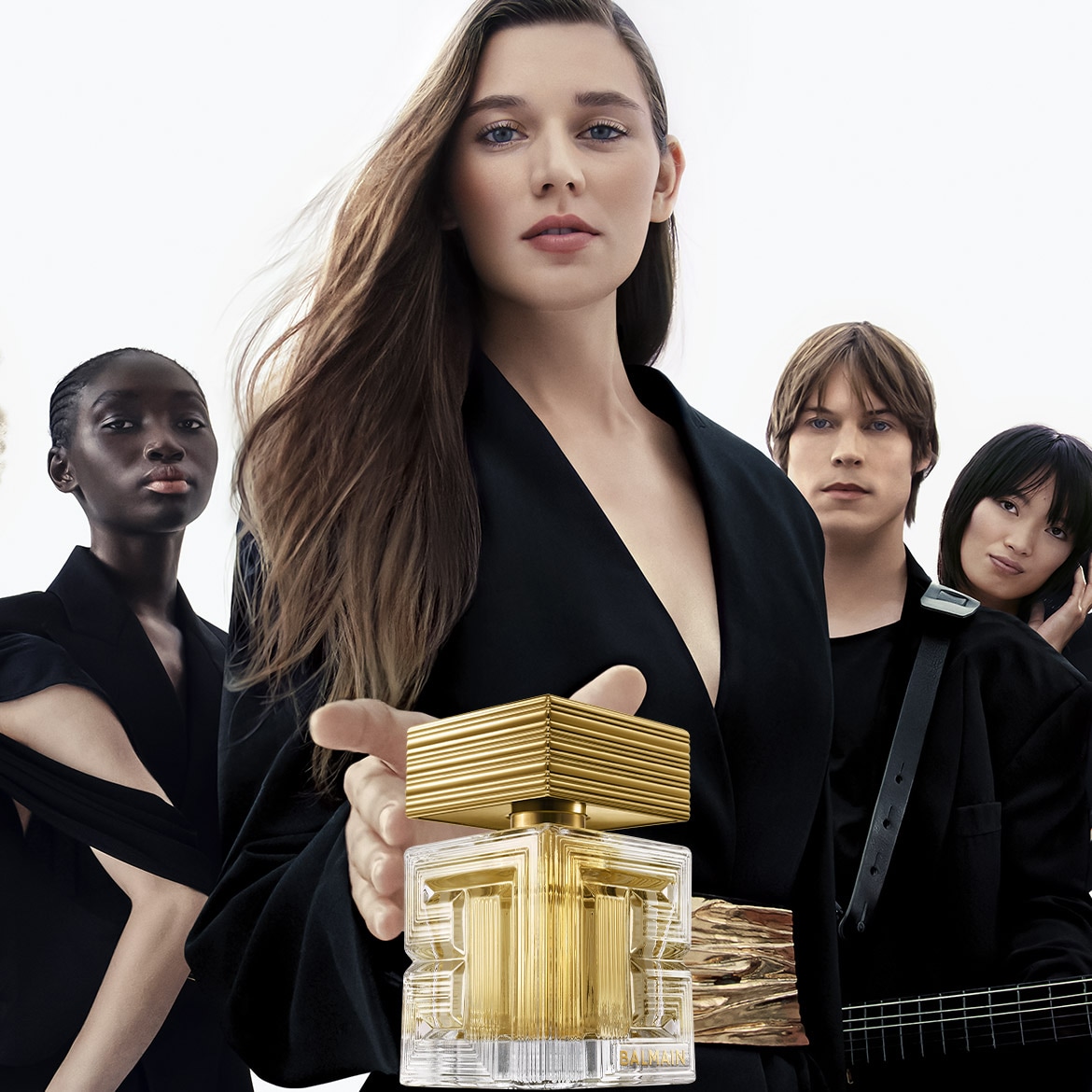 Une femme tient un parfum Balmain au flacon doré distinctif, entourée d'un groupe diversifié de personnes élégantes en noir.