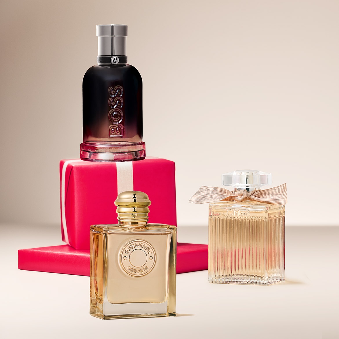 Découvrez un trio de parfums exquis : Boss, présenté sur un élégant paquet cadeau rouge, Burberry Goddess au flacon doré, et Chloé, orné d'un délicat ruban.