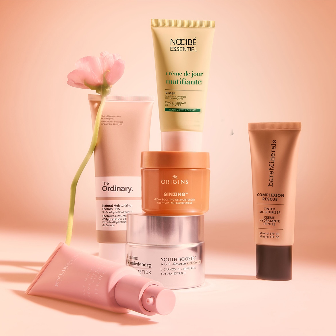 Découvrez une sélection de soins hydratants : The Ordinary, Origins Ginzing, Nocibé Essentiel, Bare Minerals, Susanne Kaufmann et Kylie Skin, présentés avec une fleur délicate.