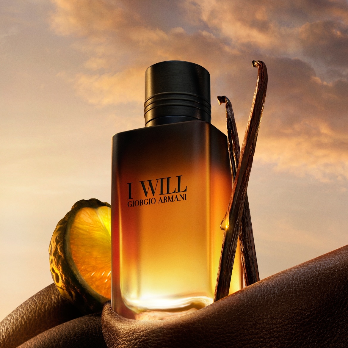 Le parfum Giorgio Armani "I Will" est présenté dans un flacon rectangulaire ambré avec un bouchon noir, accompagné d'une tranche de citron vert et de gousses de vanille, le tout sur un fond de ciel nuageux au coucher du soleil.
