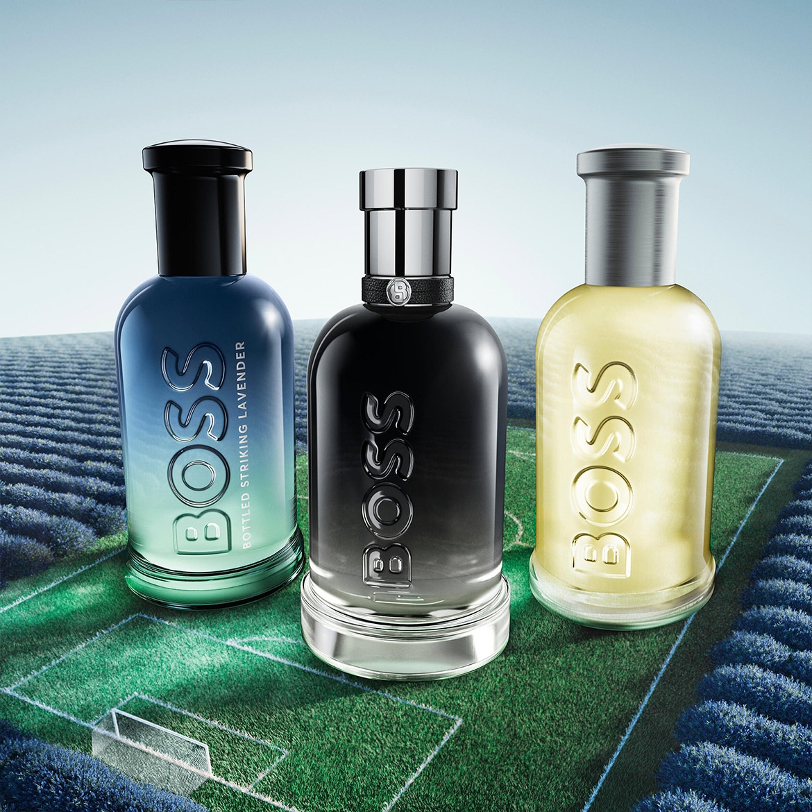 Découvrez le trio de parfums BOSS : Bottled Striking Lavender, une fragrance bleue et verte, une noire et une jaune, chacune portant le logo BOSS en relief, sur un terrain de football entouré de lavande.