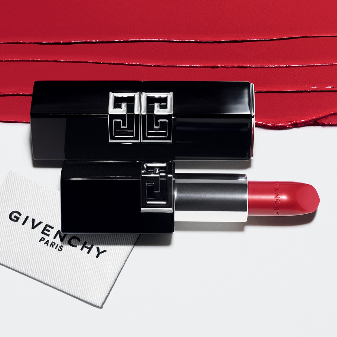 Le rouge à lèvres Givenchy Le Rouge Interdit Intense Silk est présenté avec son capuchon noir brillant orné du logo argenté, à côté du tube de rouge à lèvres rouge vif, sur un fond blanc avec des traces de rouge à lèvres.