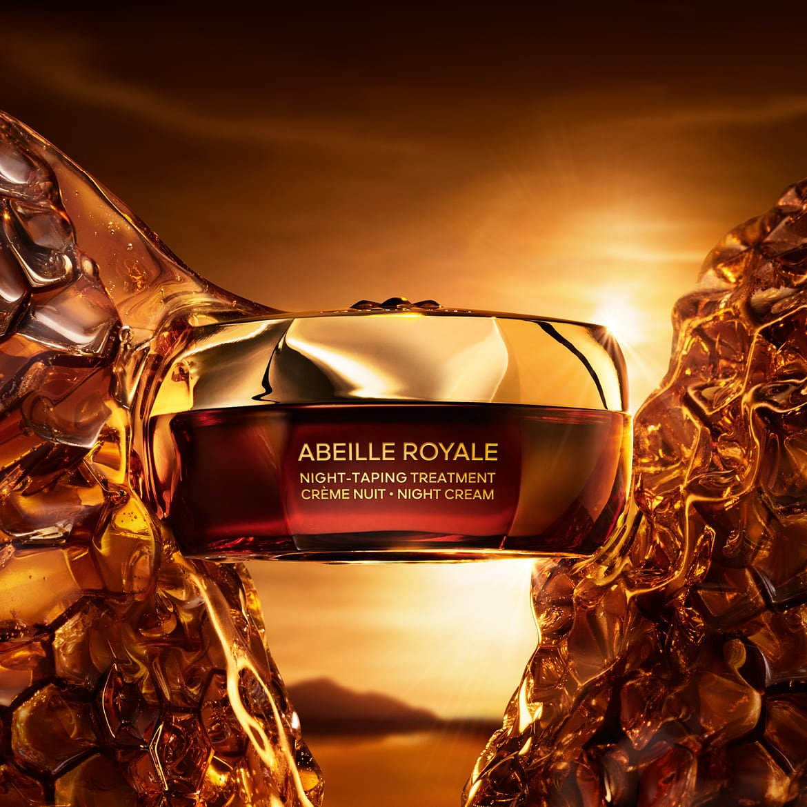 Le pot de crème de nuit Abeille Royale est mis en valeur par des formes ambrées et un coucher de soleil doré en arrière-plan, avec le texte "ABEILLE ROYALE NIGHT-TAPING TREATMENT CRÈME NUIT • NIGHT CREAM" sur le devant.