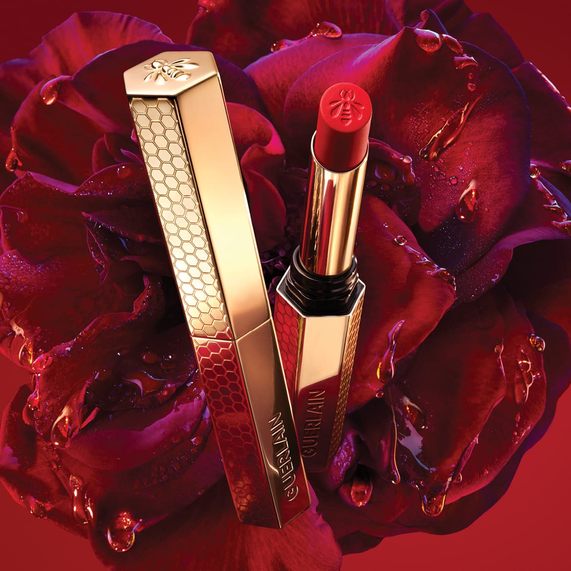 Découvrez le rouge à lèvres Guerlain Rouge G, un écrin doré orné d'une abeille, symbole de luxe et d'élégance, sur un lit de pétales de rose rouge.