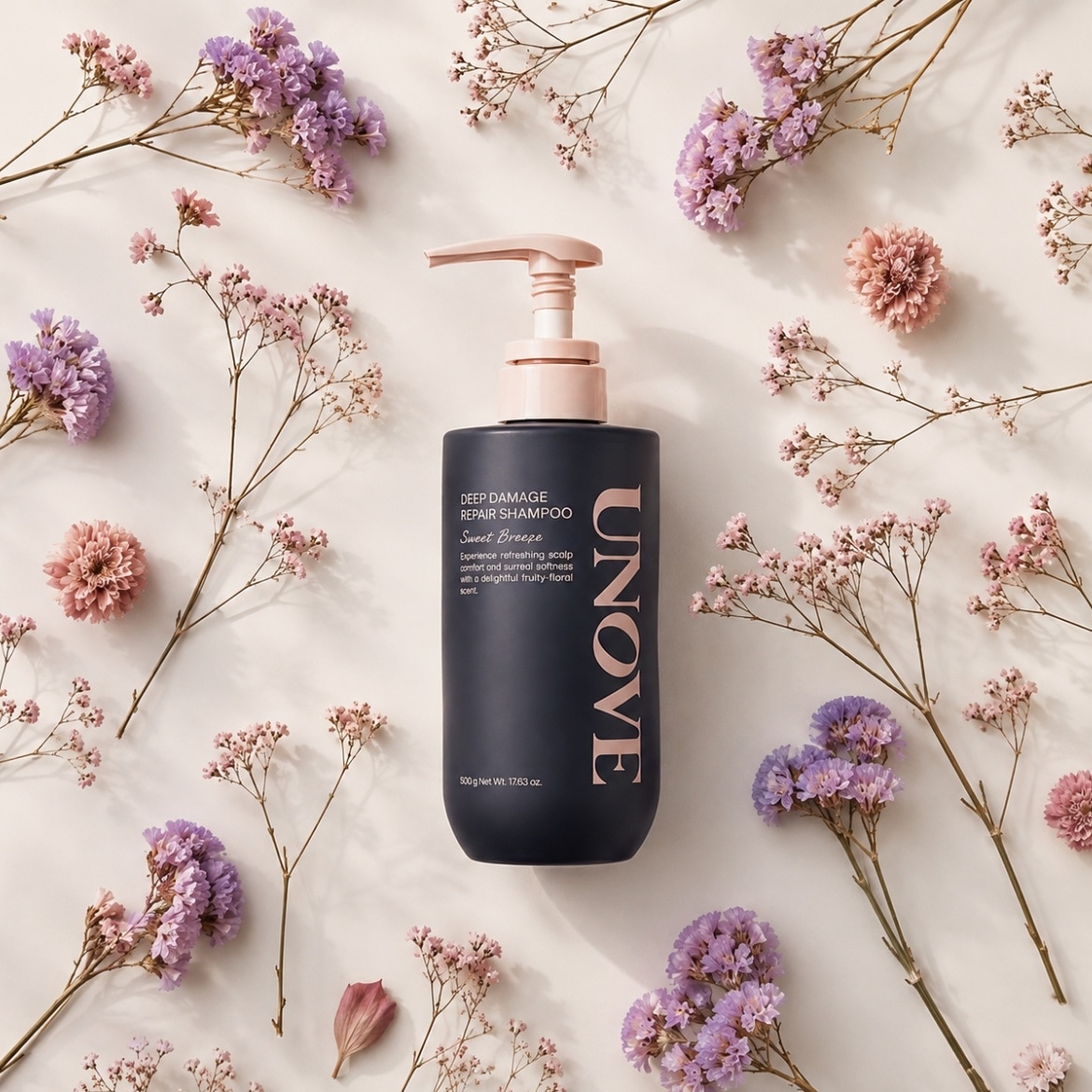 Le shampoing réparateur UNOVE Deep Damage Sweet Breeze, présenté dans une bouteille noire mate avec une pompe rose pâle, est entouré de délicates fleurs séchées violettes et roses, offrant une expérience rafraîchissante et un parfum fruité-floral.
