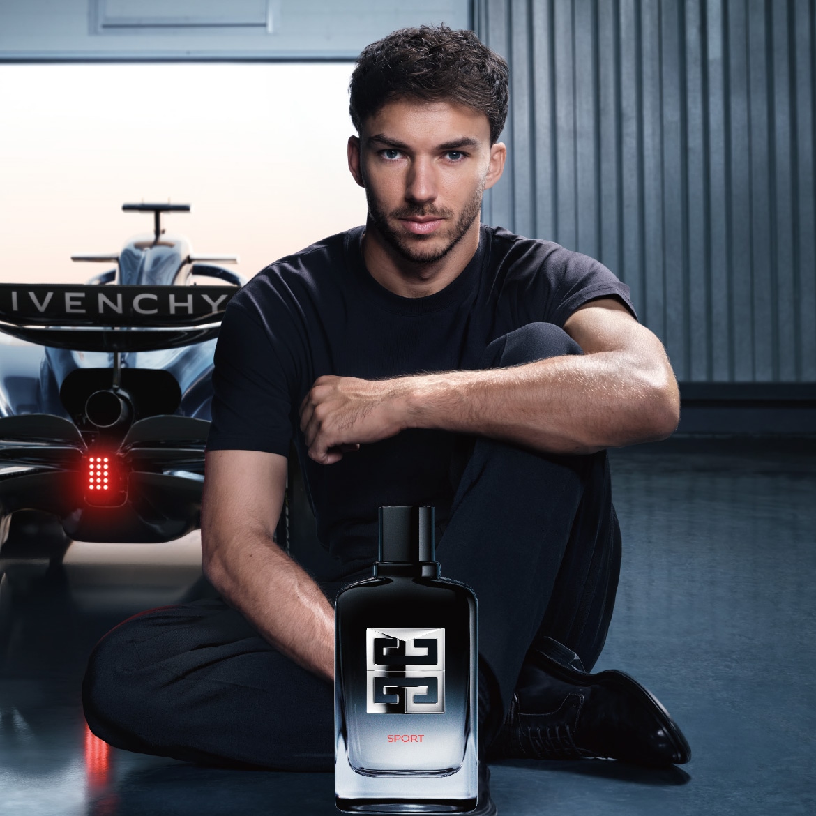 Un homme est assis devant une voiture de course, avec un flacon de Givenchy Sport au premier plan, évoquant la vitesse et l'élégance.