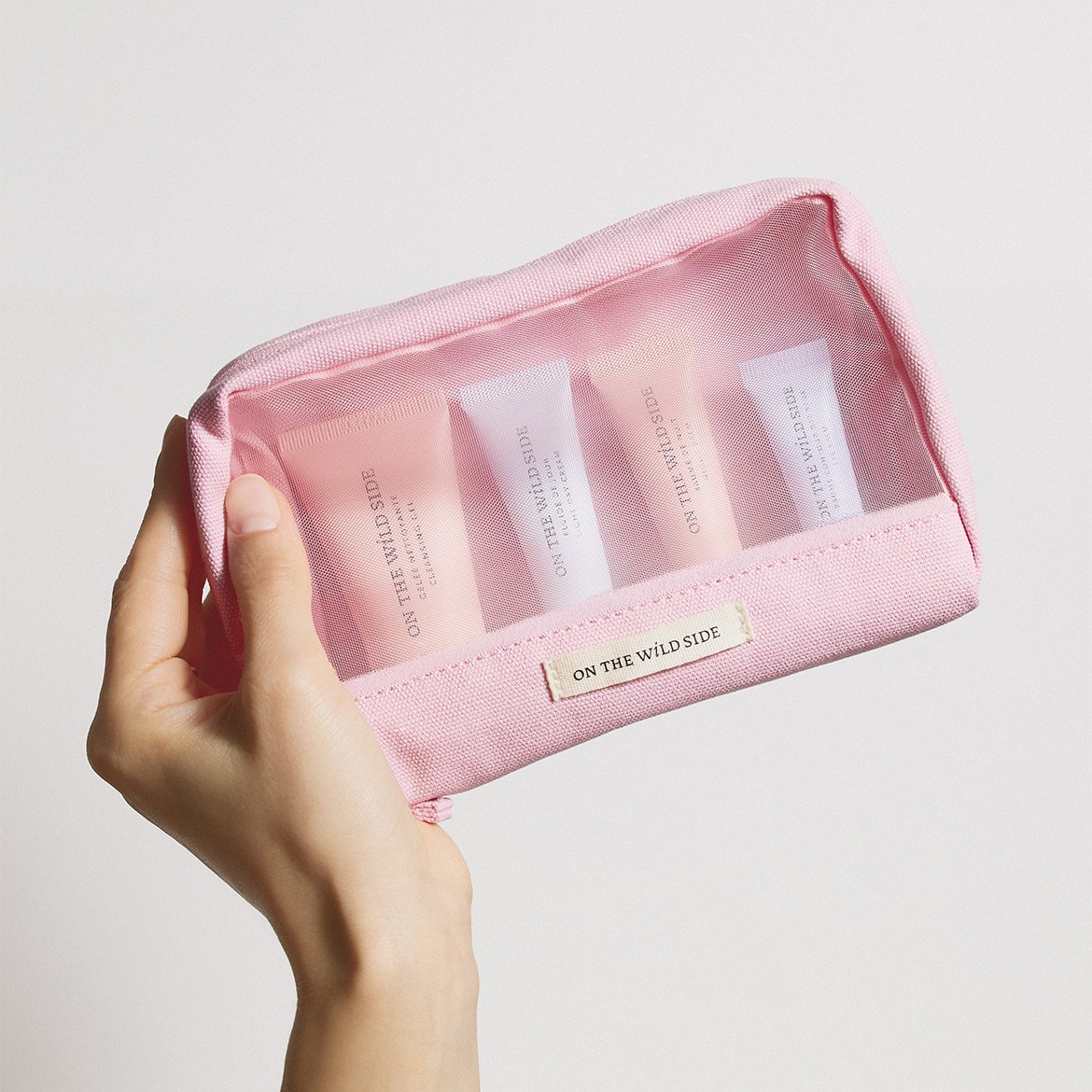 Voici une trousse de toilette rose transparente "ON THE WILD SIDE" contenant des tubes de gel nettoyant, de fluide de jour et de baume à lèvres.