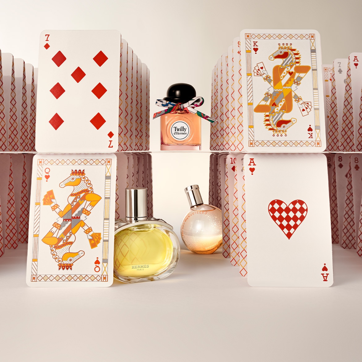Découvrez le parfum Twilly d'Hermès dans un flacon pêche orné d'un ruban coloré, entouré de cartes à jouer.