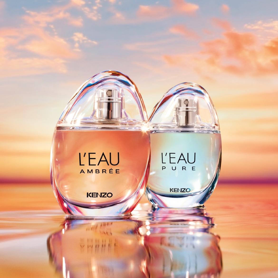 Deux flacons de parfum Kenzo, l'un ambré et l'autre bleu clair, sont posés sur une surface réfléchissante avec un ciel nuageux aux couleurs du coucher de soleil en arrière-plan.