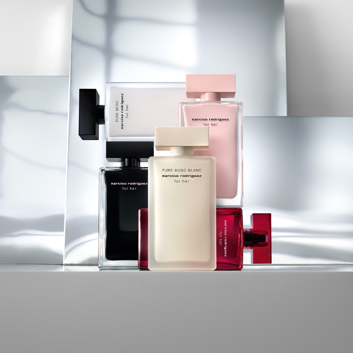 Découvrez la collection de parfums Narciso Rodriguez For Her, avec des flacons élégants en noir, blanc, rose pâle et rouge vif, chacun avec un capuchon assorti, présentés sur un fond gris clair.