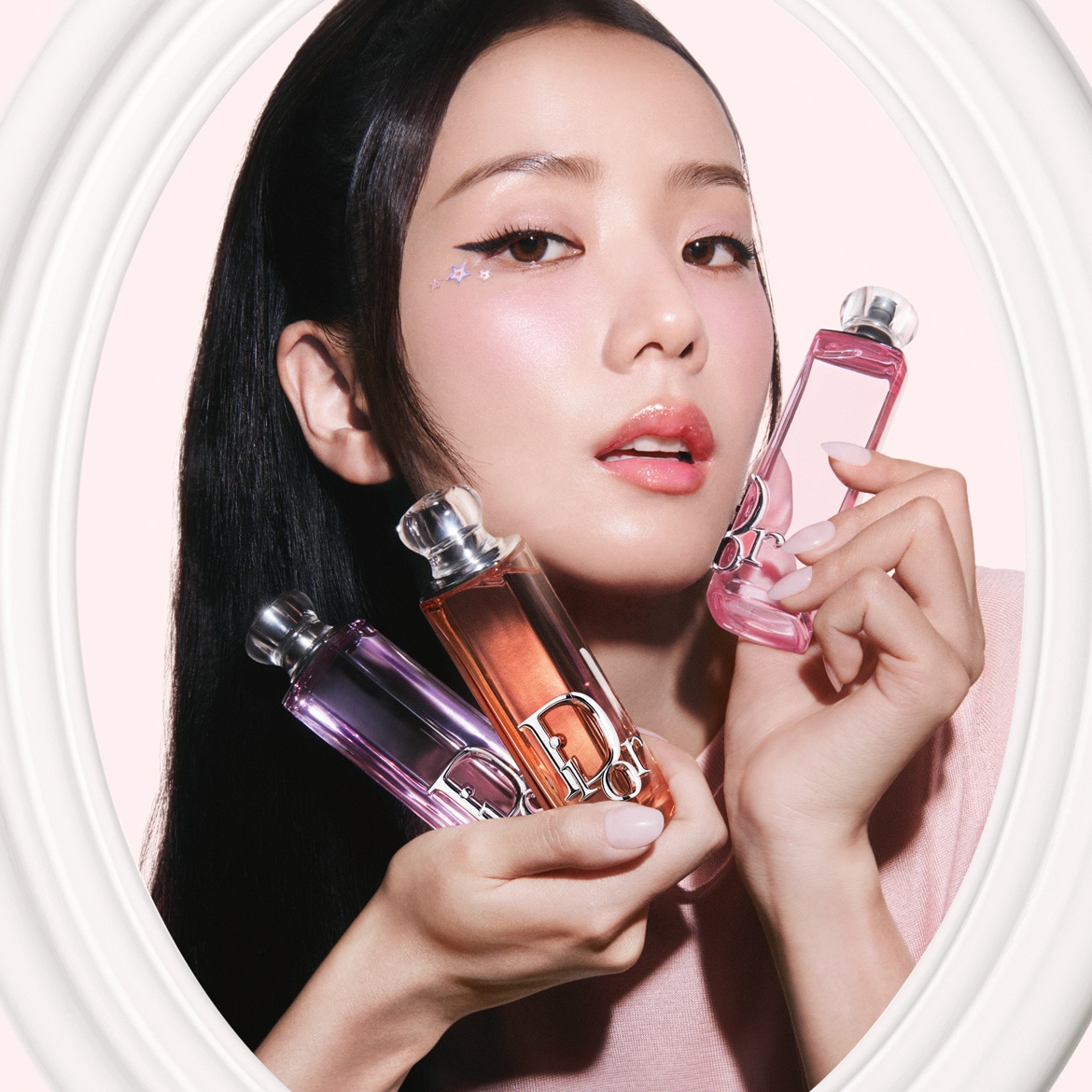 Une femme tient trois flacons de parfum Dior aux teintes rose, orange et violet, présentés dans un cadre ovale blanc pour une touche d'élégance.
