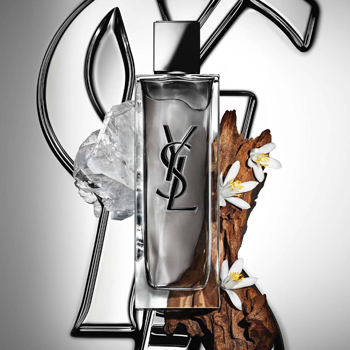 Découvrez le parfum Y de Yves Saint Laurent, un parfum frais et élégant pour homme, présenté dans un flacon transparent orné du logo YSL noir, accompagné d'un cristal, de fleurs blanches et d'un morceau de bois.