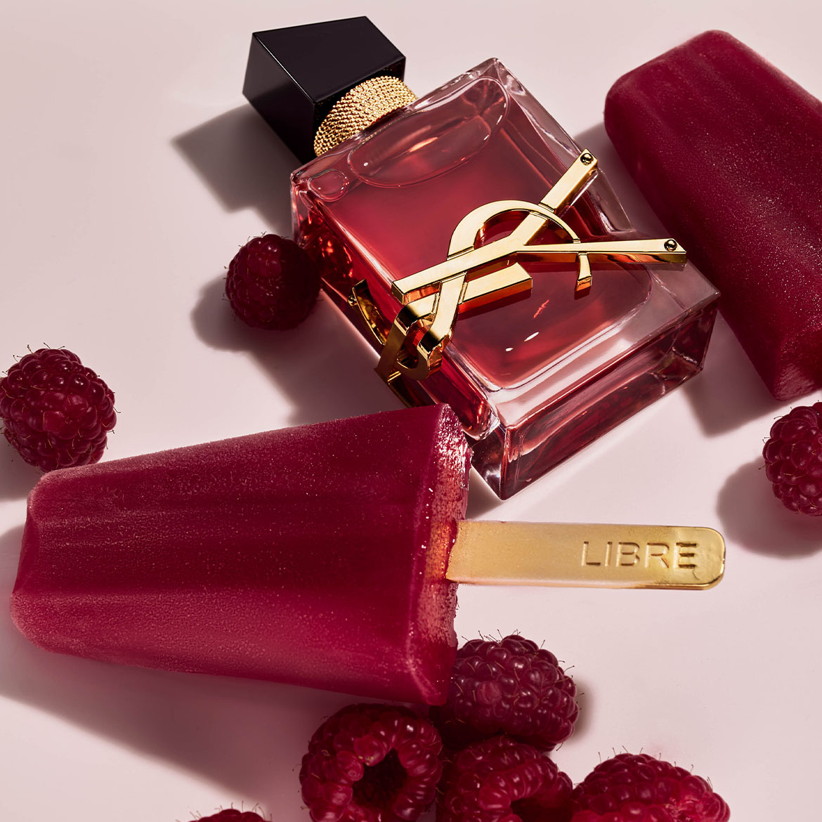 Découvrez le parfum Yves Saint Laurent Libre dans un flacon rouge rubis, accompagné de framboises fraîches et de bâtonnets glacés portant l'inscription 'Libre'.