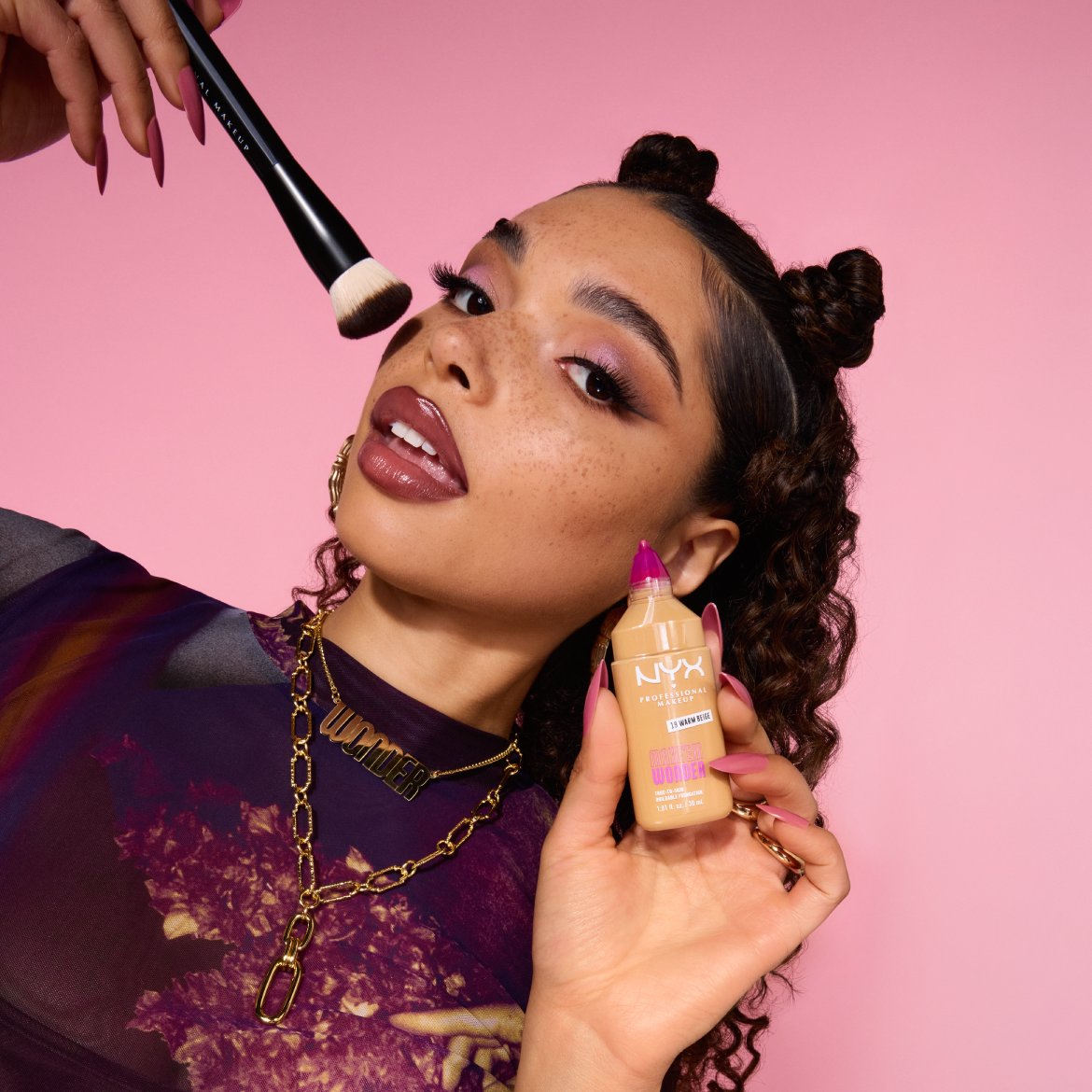 Une femme utilise un pinceau de maquillage et tient un fond de teint NYX Professional Makeup Teint Lingerie Wonder en teinte 11 Warm Beige.