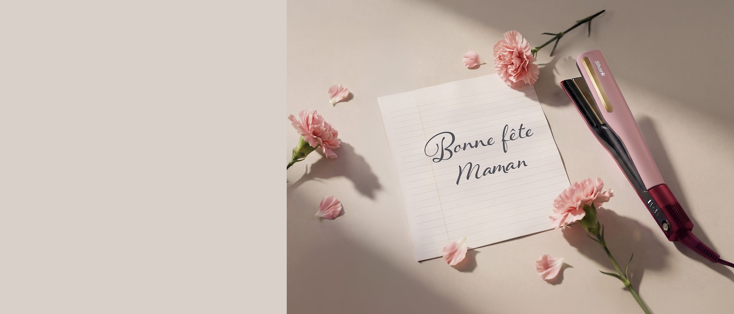 Une carte avec l'inscription calligraphiée « Bonne fête Maman » est entourée d'œillets roses et d'un lisseur à cheveux rose et bordeaux.