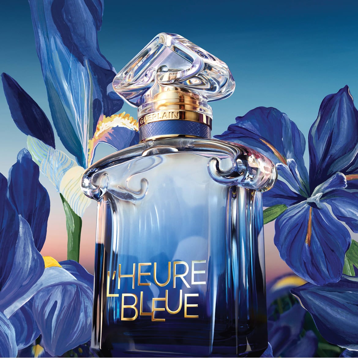 Le parfum L'Heure Bleue de Guerlain est présenté dans un flacon en verre dégradé de bleu, orné d'un bouchon sculpté et entouré de fleurs d'iris bleues.