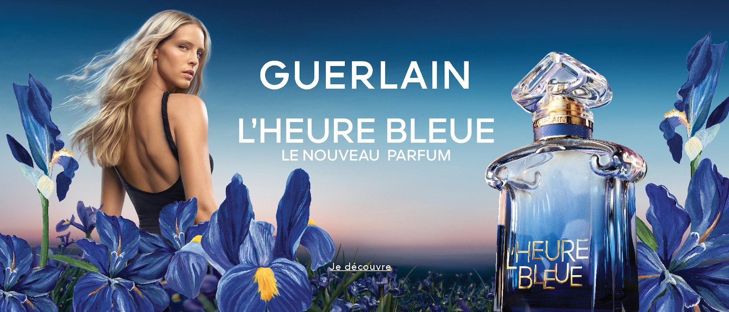 Découvrez le nouveau parfum L'Heure Bleue de Guerlain, présenté avec une femme blonde aux cheveux flottants et des fleurs d'iris bleues.