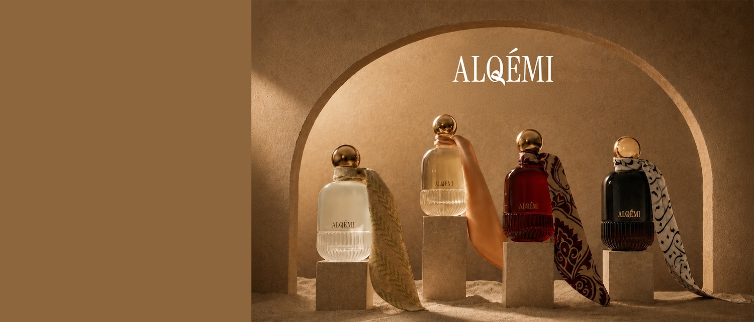 Quatre flacons de parfum ALQÉMI sont présentés dans une arche de couleur sable, chacun avec un bouchon doré et un foulard en soie noué autour du col, sur un fond marron.