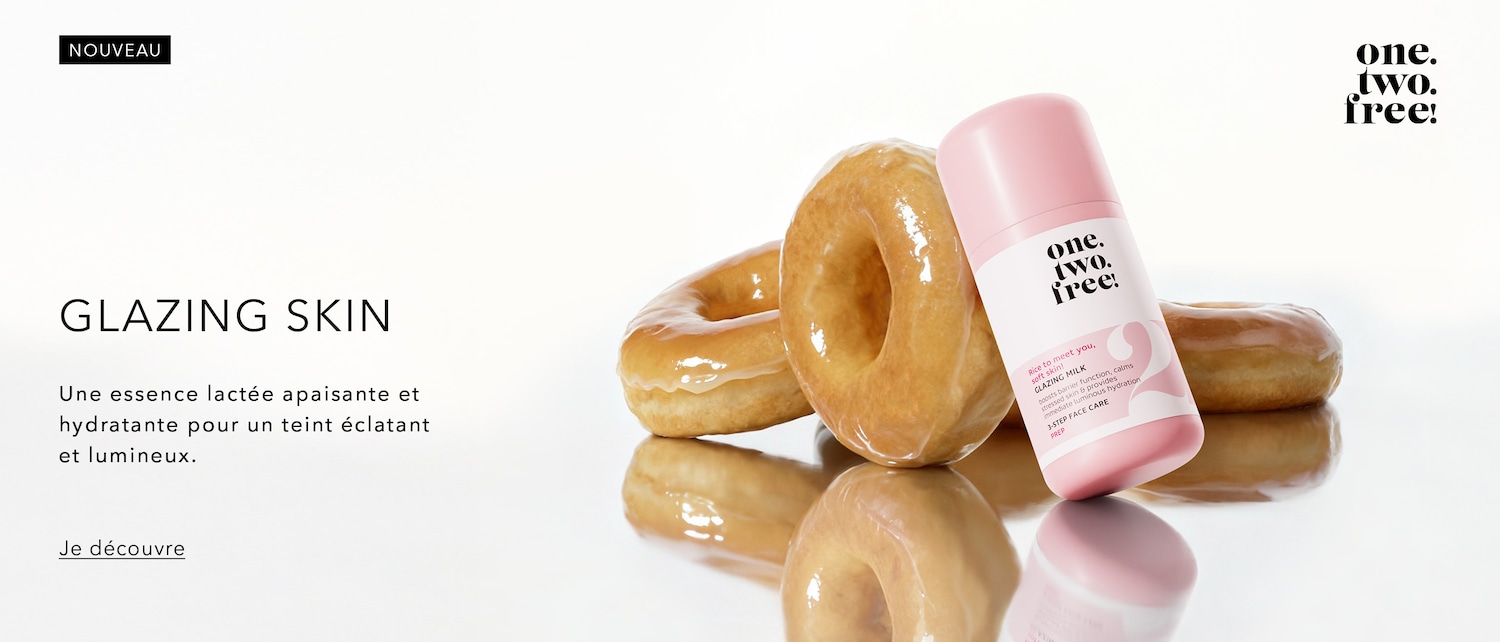 Découvrez le nouveau Glazing Skin de one. two. free!, une essence lactée apaisante et hydratante pour un teint éclatant et lumineux, présentée dans un flacon rose à côté de beignets glacés.