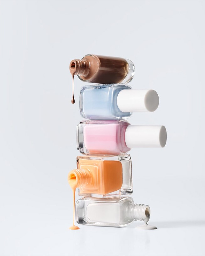 Une pile ludique de vernis à ongles dans des tons pastel et neutres, certains renversés pour montrer les couleurs riches et crémeuses.