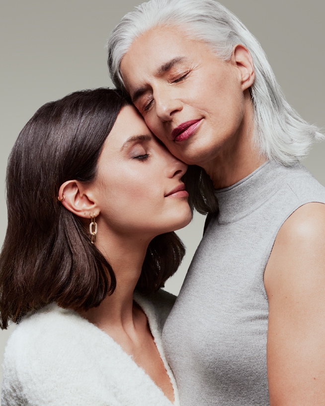 Gros plan sur une jeune femme brune et une femme plus âgée aux cheveux gris, les yeux fermés, se tenant tendrement l'une contre l'autre.