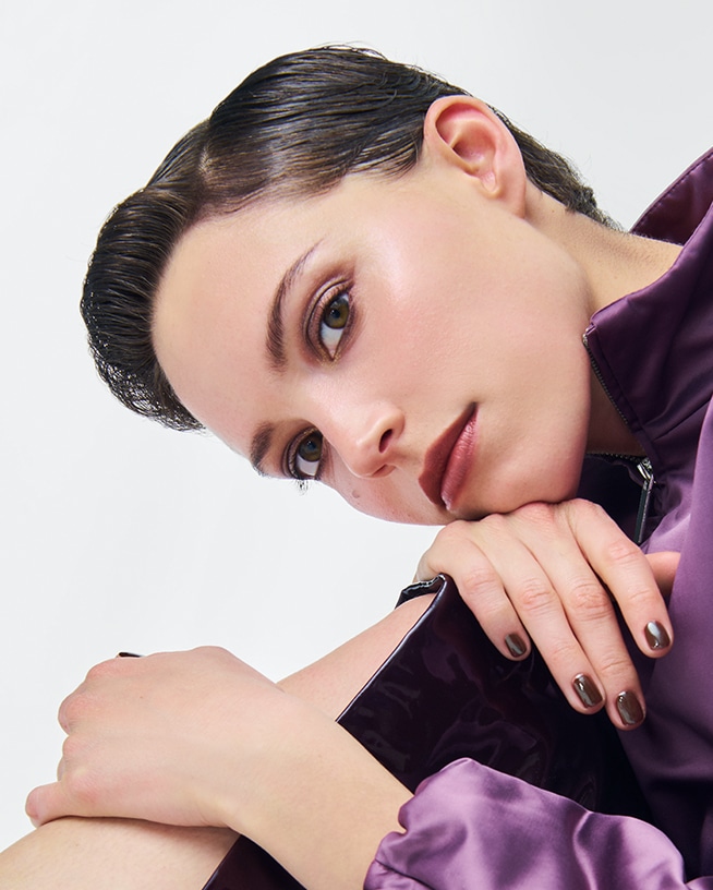 Gros plan d’une personne portant un maquillage automnal et un vernis à ongles foncé sur fond clair. L’image évoque les tendances maquillage et les inspirations beauté de la saison automnale.