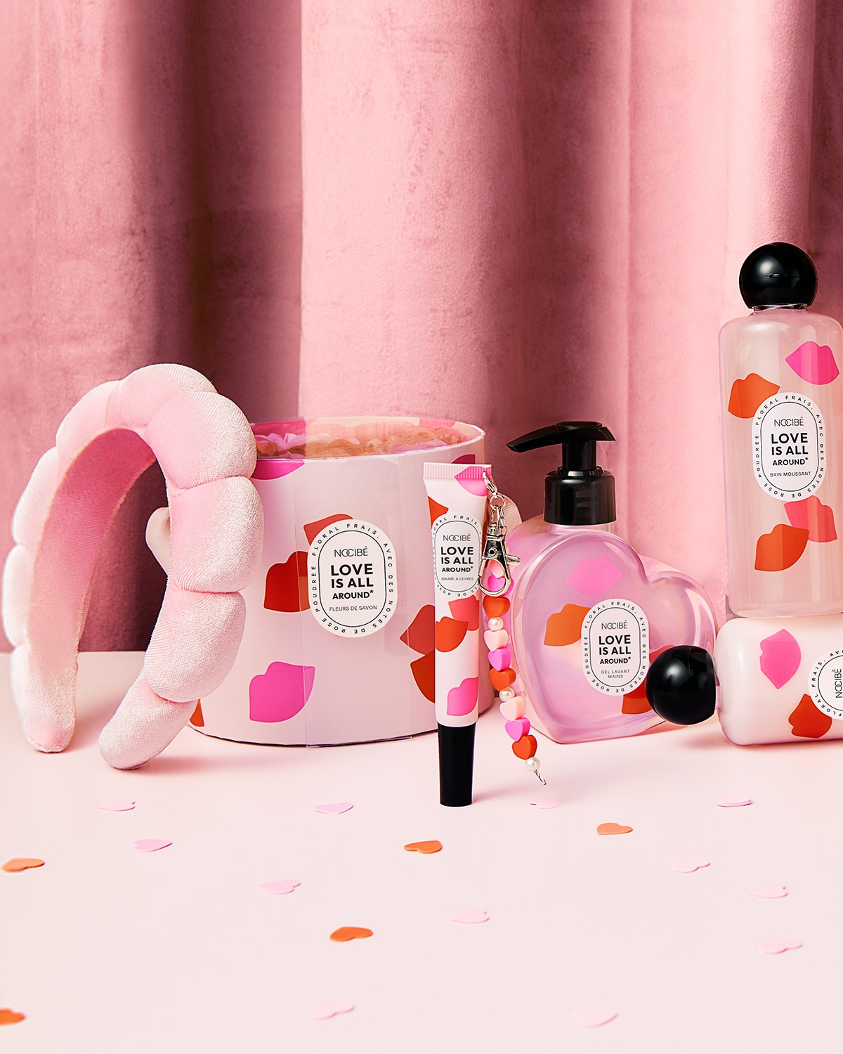 Découvrez l'univers rose poudré de Nocibé avec des produits de soin portant la mention 'Love is all around', incluant un bandeau, un gel lavant et un bain moussant.