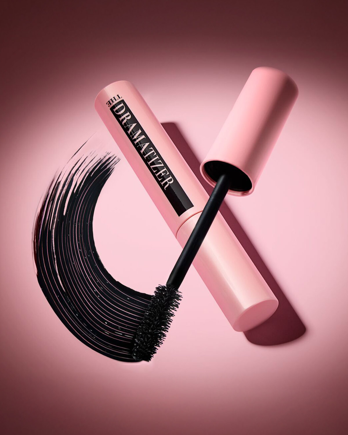 Voici le mascara The Dramatizer dans son tube rose pâle, accompagné de sa brosse noire et d'une touche de mascara noir créant un effet dramatique.