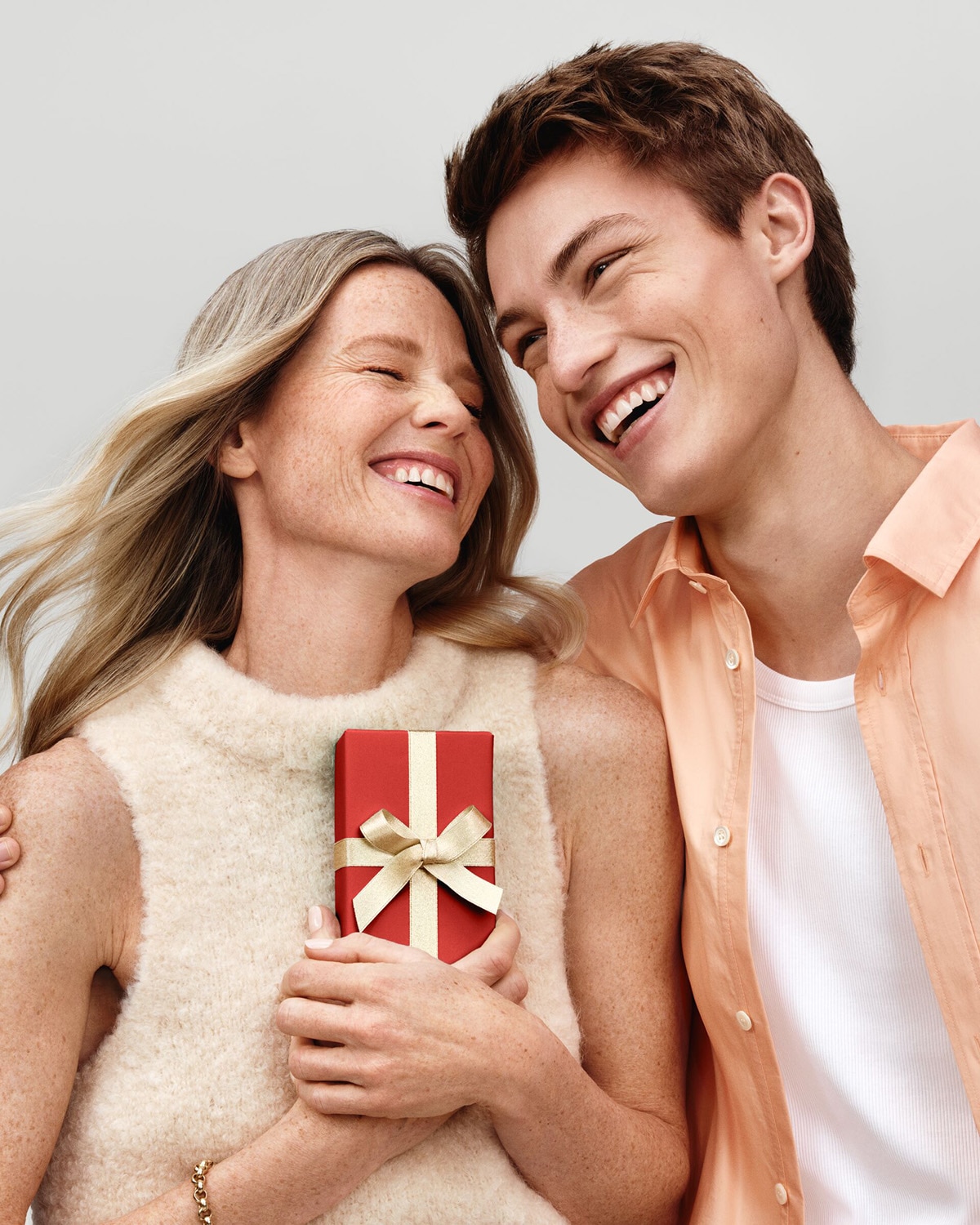 Un jeune homme et une femme sourient en tenant un cadeau emballé dans du papier rouge et un ruban doré, rayonnant de joie.
