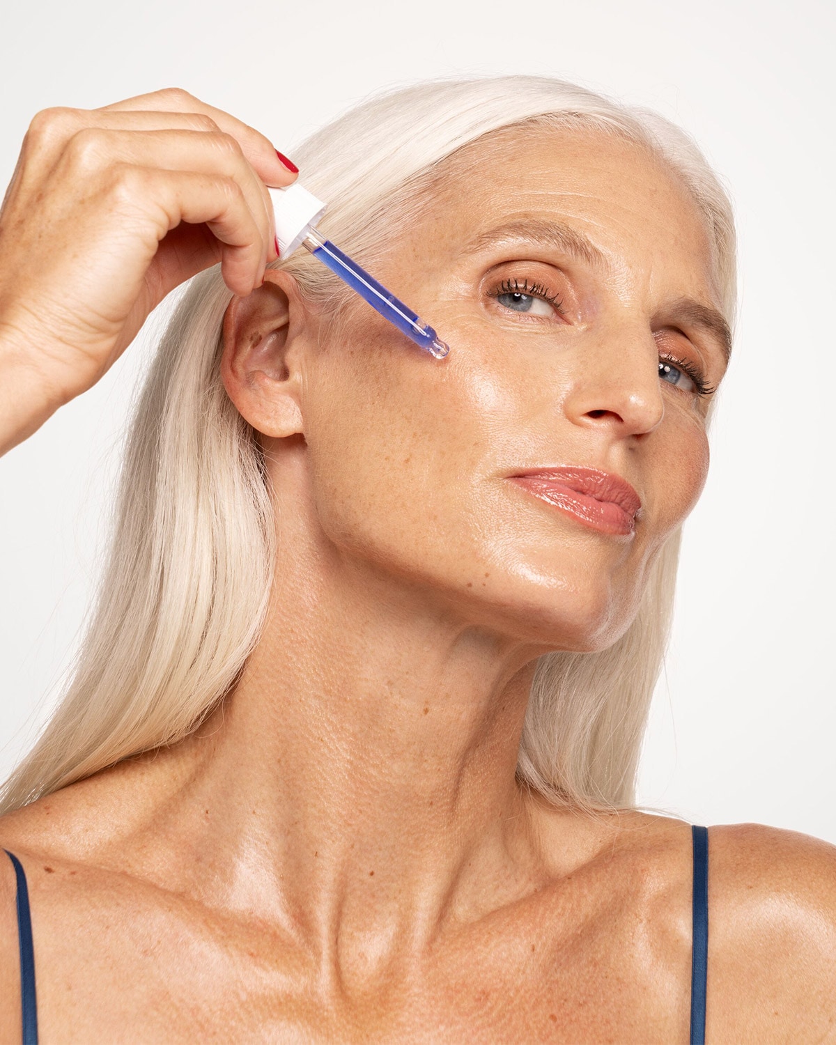 Une femme d'âge mûr aux cheveux blancs applique un sérum bleu sur sa peau pour l'hydrater et lui donner un éclat de jeunesse.