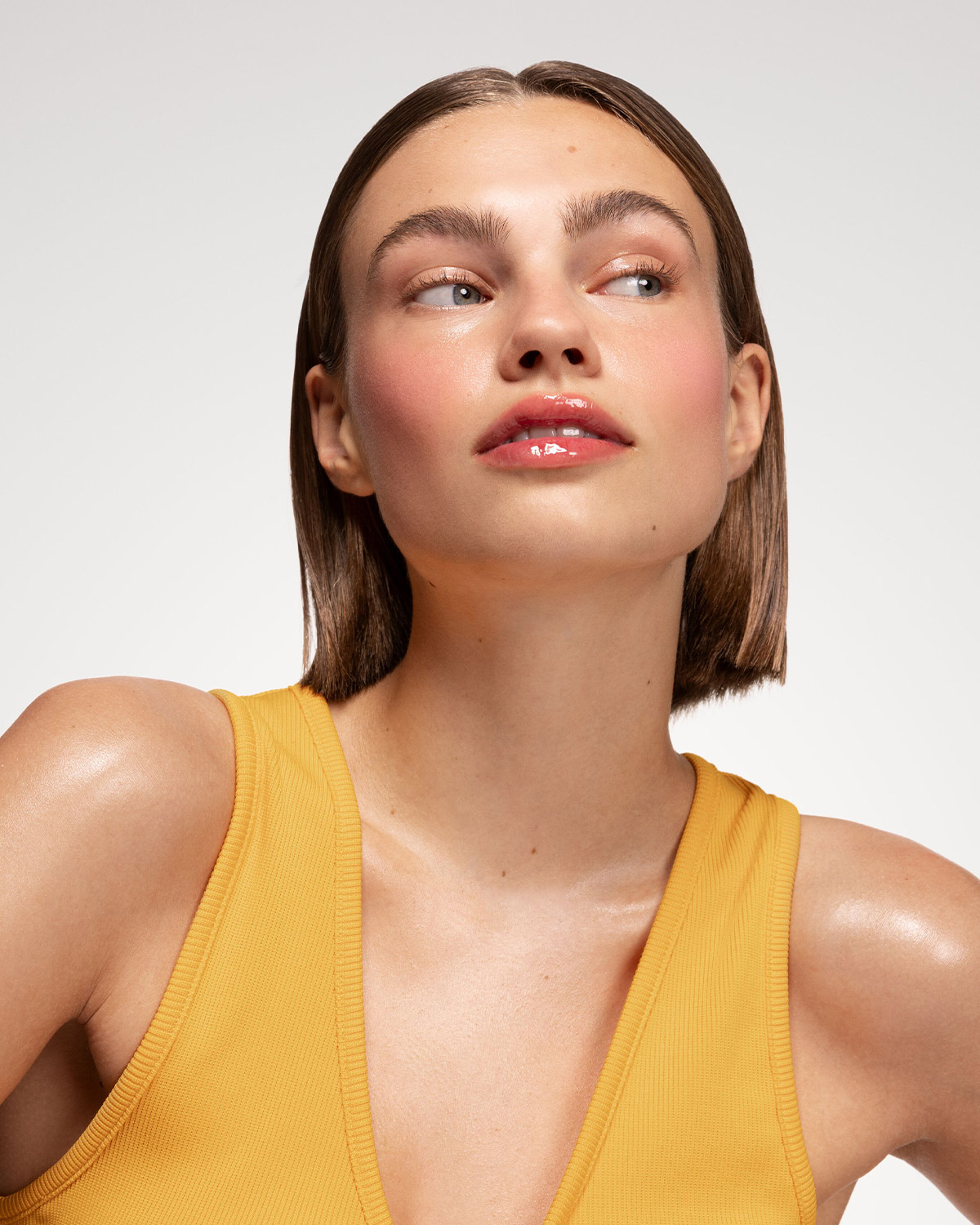 Découvrez un teint éclatant avec un blush rosé et des lèvres brillantes, le tout sublimé par un débardeur jaune.
