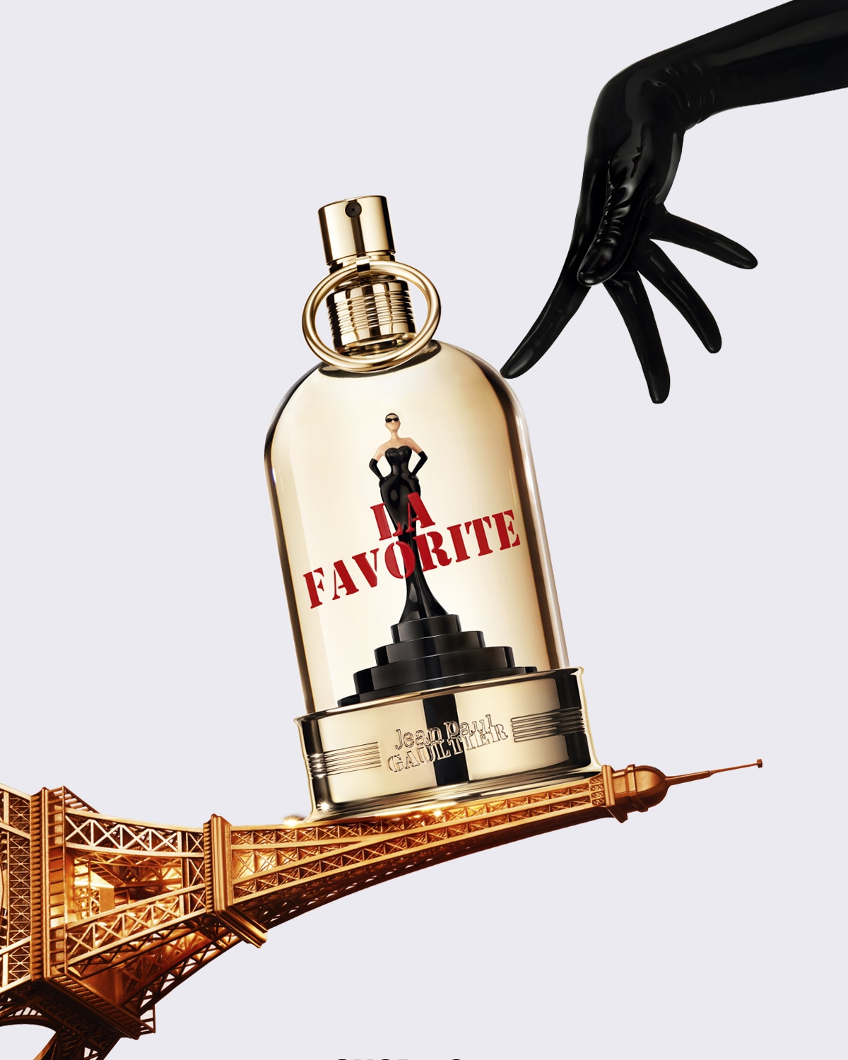 Le parfum "La Favorite" de Jean Paul Gaultier est présenté dans un flacon doré en forme de trophée, avec une figurine féminine en robe noire et l'inscription "La Favorite" en rouge, le tout posé sur la Tour Eiffel.