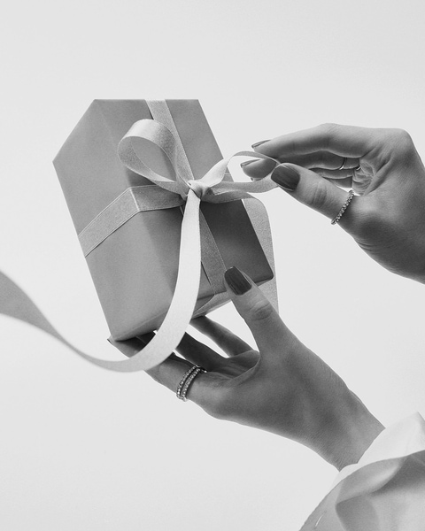 Les mains défont délicatement le ruban d'un cadeau emballé dans une boîte élégante, promesse d'une surprise.